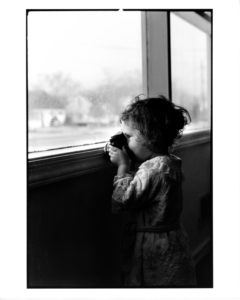 young girl looks out window through toy camera